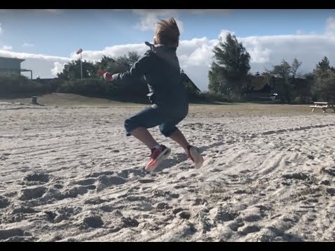 Kind springt auf Sandstrand mit ausgebreiteten Armen vorwärts.