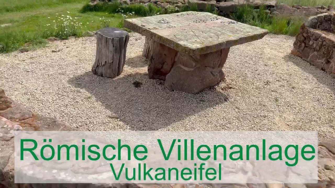 Steintisch und Holzbank auf Kiesfläche vor Ruinen der Römischen Villenanlage in der Vulkaneifel.